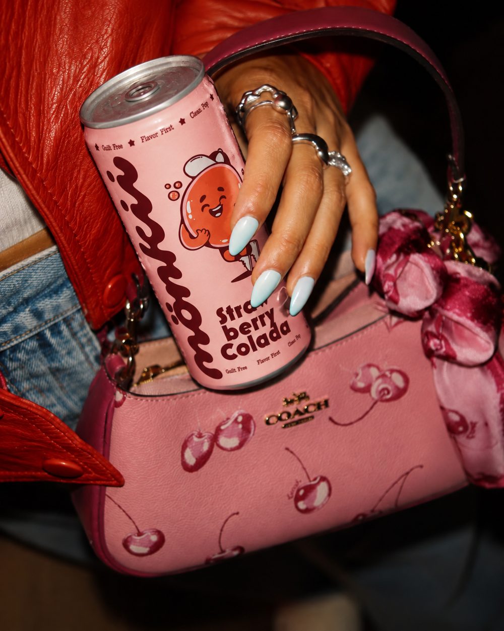 Hand holding a Strawberry Colada can against a pink shoulder bag