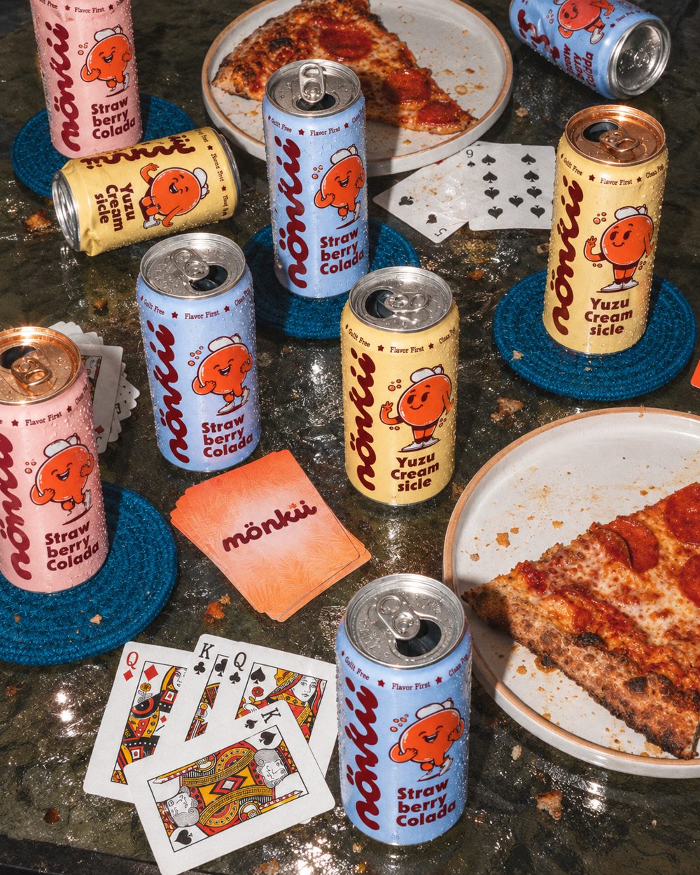 Mönkii cans on a table with pizza and a card game